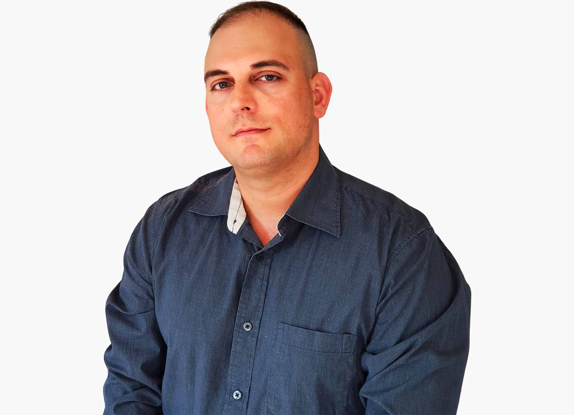 Confident man in a casual blue shirt posing against a white background.