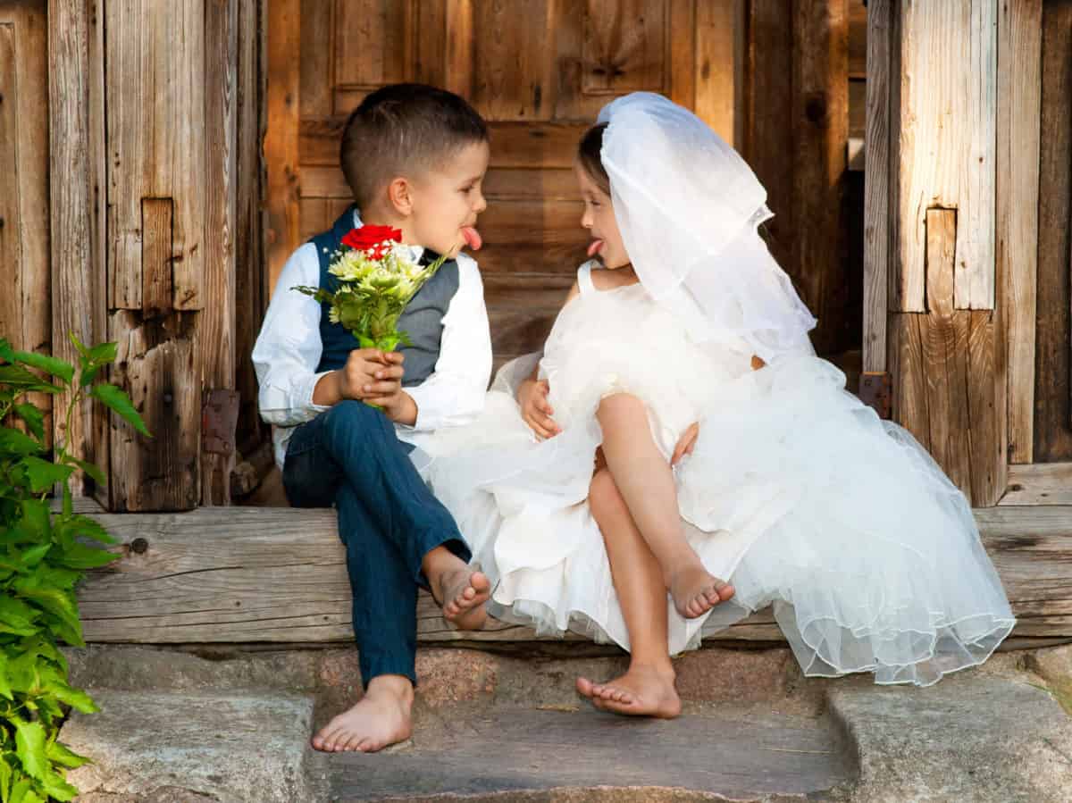 Childhood innocence: two young children engage in playful imitation of a wedding, capturing a moment of pure joy and imagination on a rustic wooden doorstep.