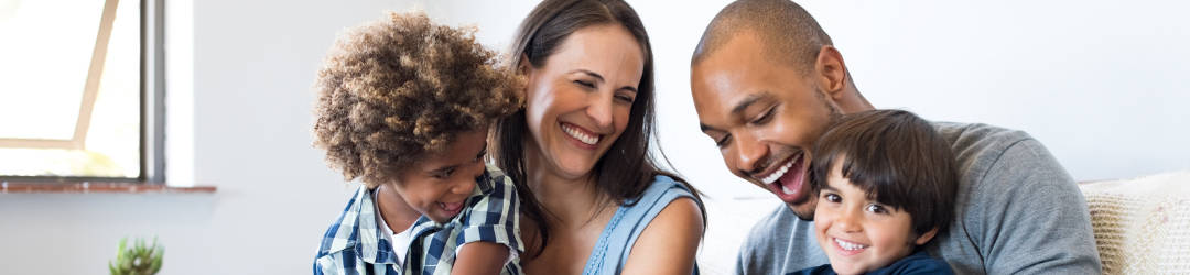 A joyful family moment with parents and two children laughing and embracing.