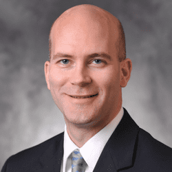 A professional portrait of a smiling bald man wearing a suit and tie.