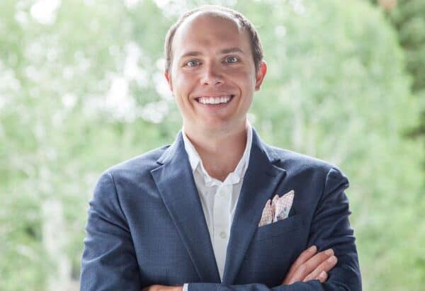 Confident businessman with a friendly smile, dressed in a blue suit with a patterned pocket square, standing outdoors.