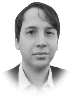 Black and white portrait of a man with medium-length hair and a collared shirt under a jacket, looking directly at the camera with a neutral expression.