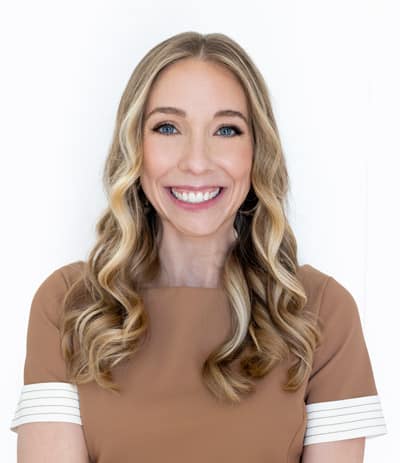 A cheerful woman with a bright smile and wavy blond hair, posing against a white background.