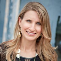 A smiling woman with blond hair posing for a professional headshot, featuring a blurred urban background.