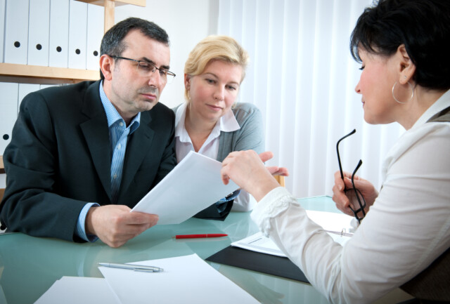 Three professionals in a meeting, with one of them presenting a document for review to her attentive colleagues.