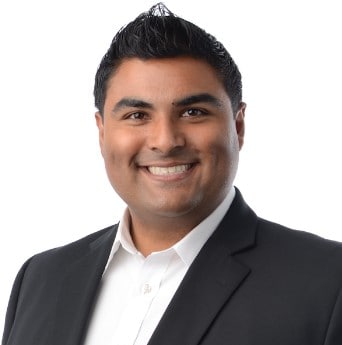 A portrait of a smiling man in professional attire, featuring a black suit jacket and white shirt, set against a clean white background.