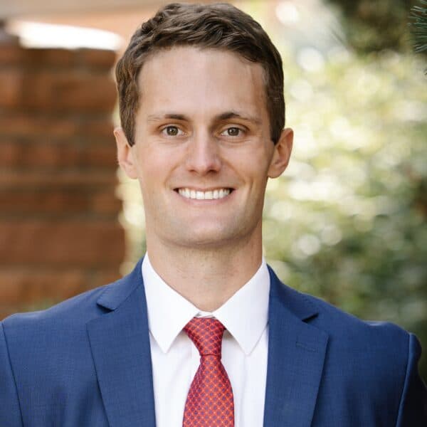 A smiling man with blond hair wearing a blue polo shirt posing for a casual outdoor portrait.
