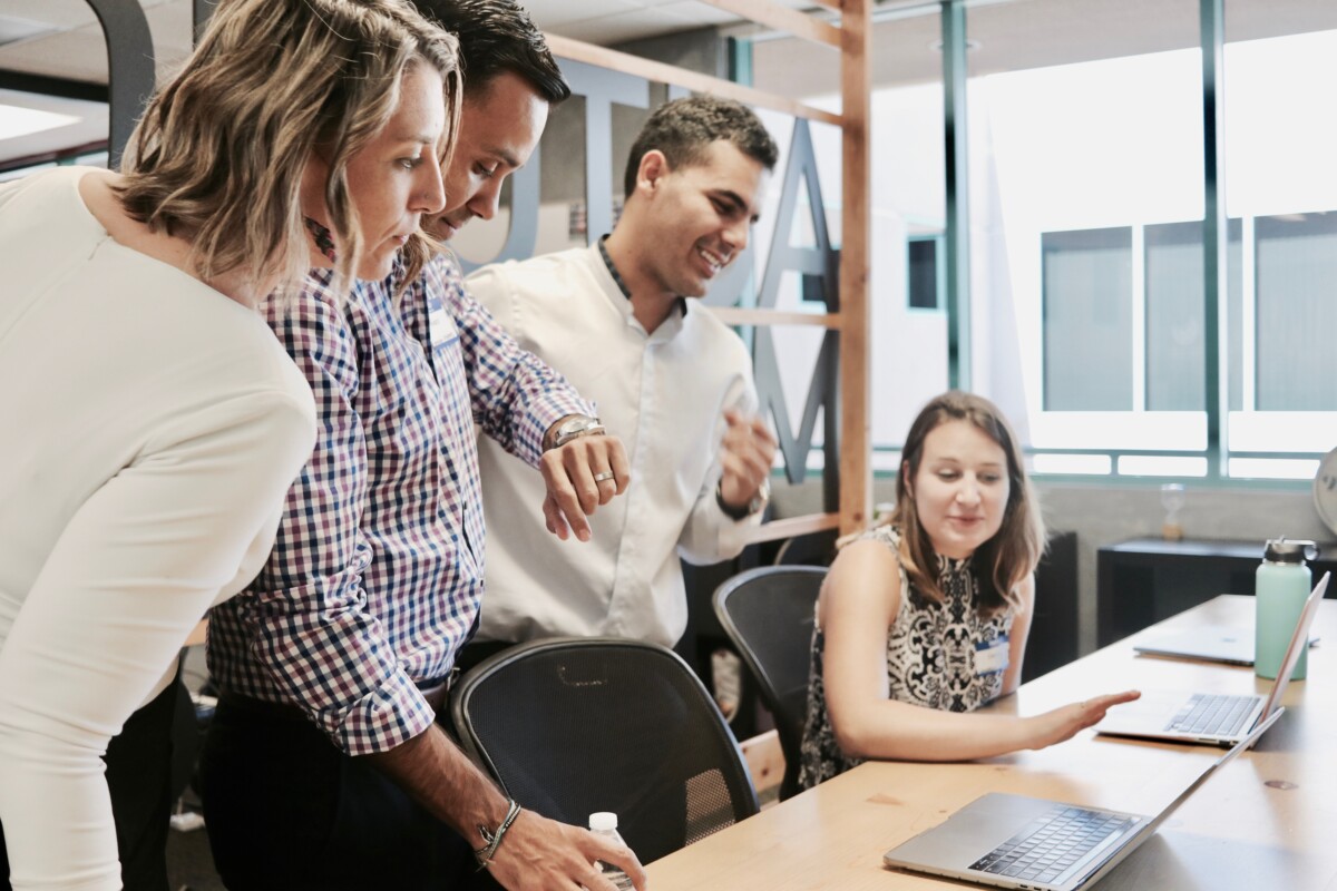 Team of colleagues engaging in a collaborative discussion with a focus on a laptop screen in a modern office setting.