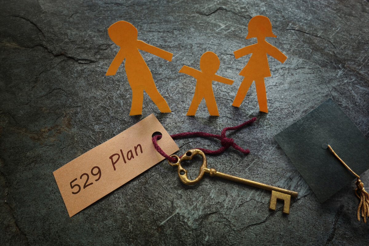 Paper cutouts of a family next to a key and a label reading "529 plan" on a textured surface, symbolizing the concept of saving for a child's education.
