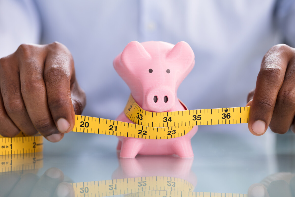 Measuring financial health: a person tightening the belt on a piggy bank signifying budgeting and saving strategies.