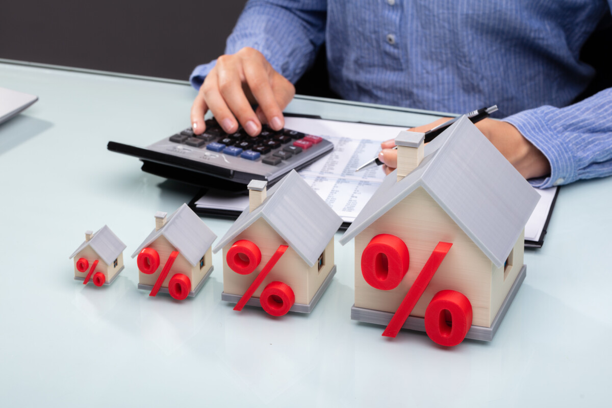 A person calculating real estate finances with house models displaying percentage symbols, suggesting a focus on interest rates or investment returns.
