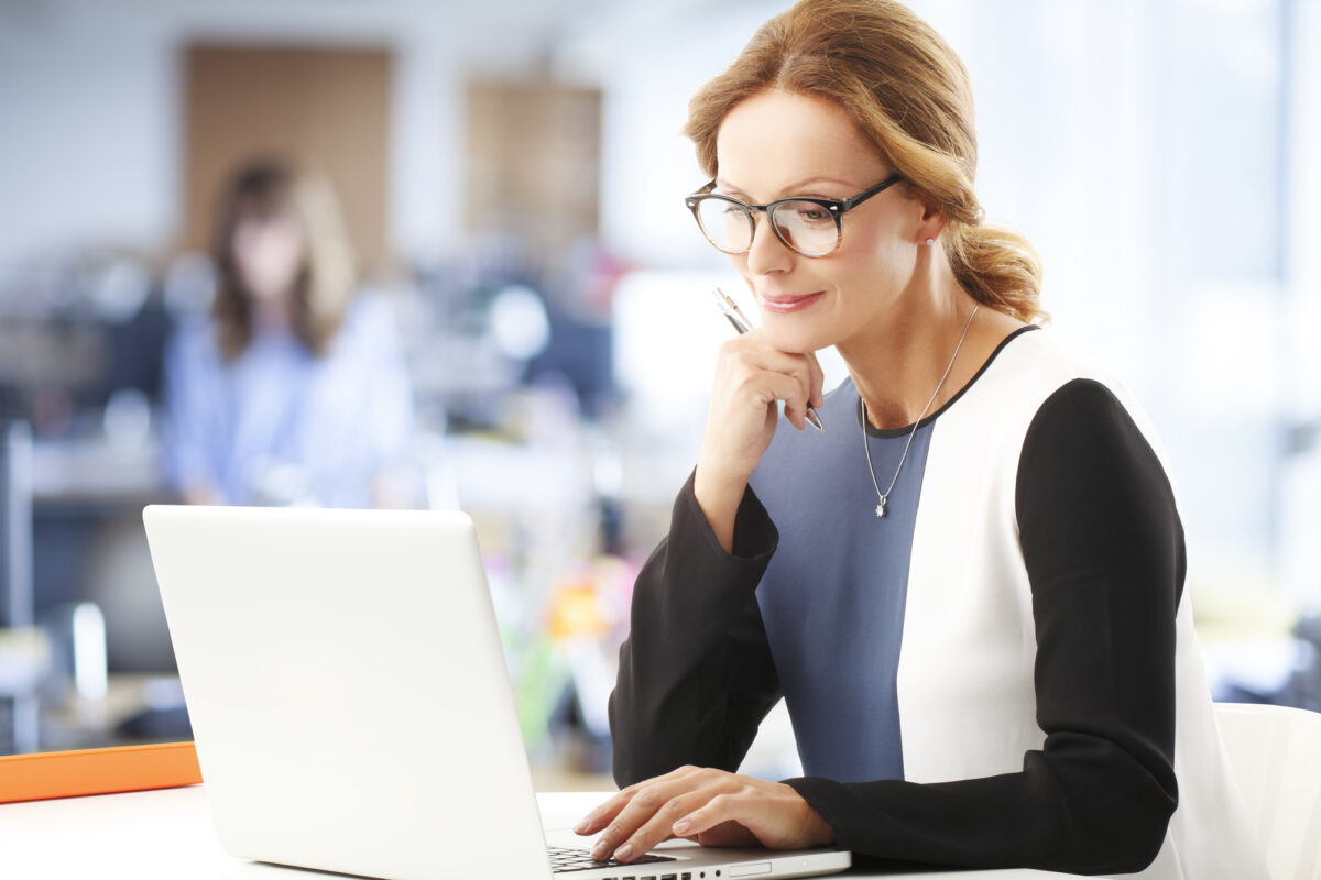Focused professional woman working intently on her laptop in a bright office environment.