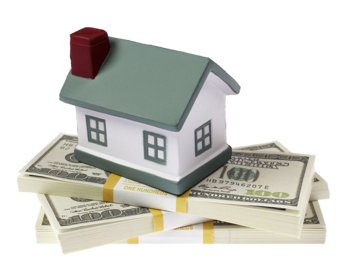 A model house placed on top of stacks of us hundred dollar bills, symbolizing real estate investment, the cost of housing, or home mortgage.