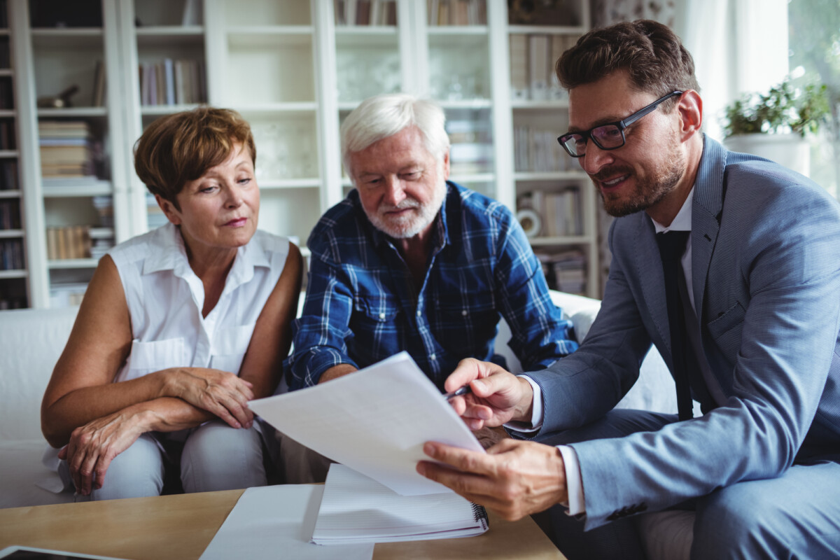 Financial advisor presenting a document to a senior couple during a consultation in a bright, modern office.
