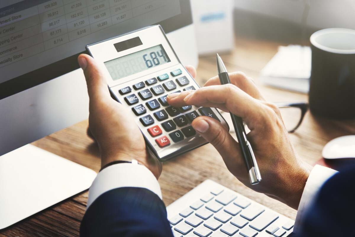 A professional working on financial calculations using a calculator with documents and a laptop on the desk.