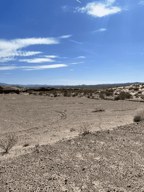 A view of arid scrubland under a vast blue sky dotted with streaky clouds.