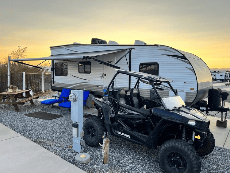 An rv parked in a quiet campsite at dusk with an off-road vehicle in the foreground, symbolizing adventure and travel.
