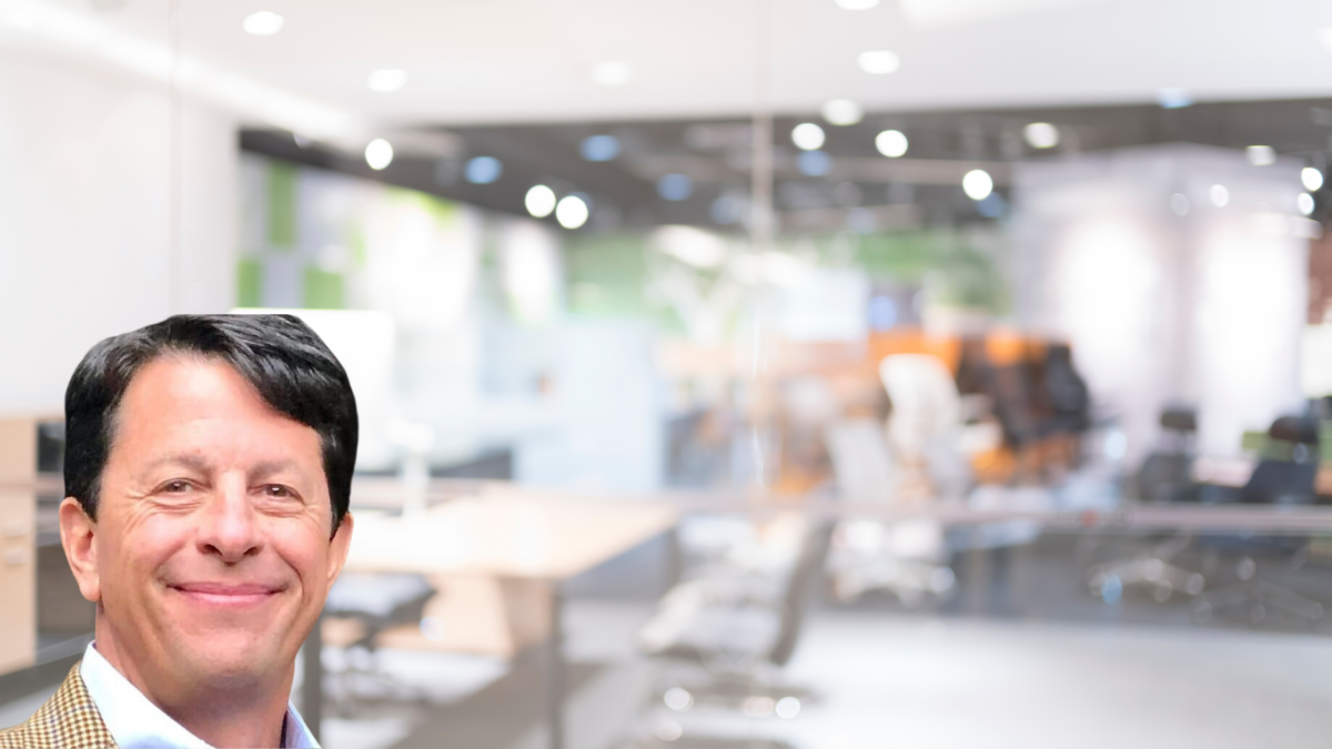 A smiling man in business attire with a modern office space blurred in the background.