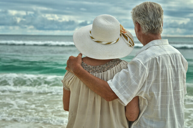 A loving, elderly couple embracing while gazing out over the serene ocean, symbolizing enduring companionship and peaceful retirement.