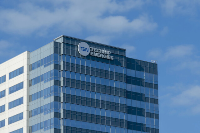 A modern glass office building with the "Technip Energies" logo and name displayed near the top, set against a blue sky with scattered clouds.